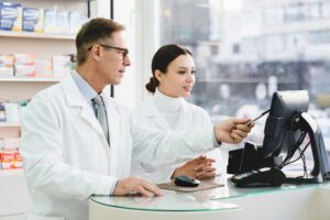 pharmacist pointing showing male colleague medication prices prescriptions on computer screen.jpg